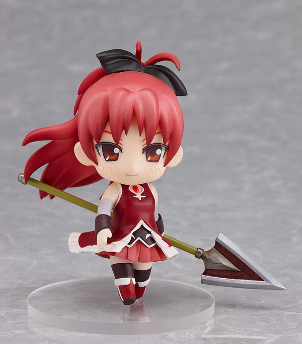 a nendoroid petit of kyouko sakura. kyouko is a girl of average height with red hair that reaches past her waist tied in a high ponytail, and crimson eyes. she is in a cute chibi style, in her magical girl outfit. her magical girl outfit consists of a dark red one-piece high-low dress with a high collar and a small cutout just below her neck that displays her red soul gem, a dark pink skirt, black socks, red knee high boots with white trim, beige arm socks and black cuffs. she is holding her weapon of choice, a spear, in a mildly relaxed pose.
