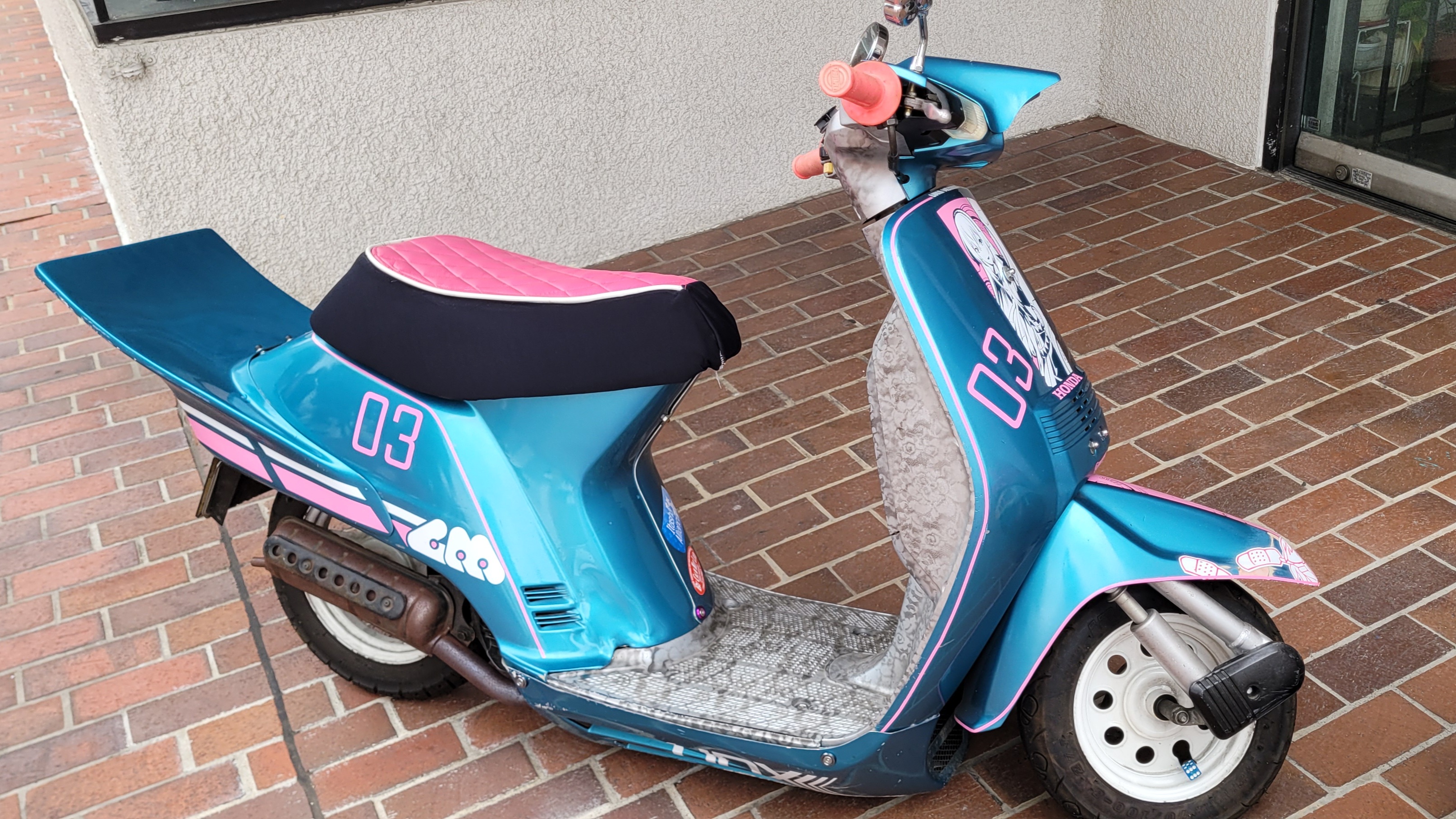 a photo of the luka itasha bike. the bike is primarily blue, with various pink and white decals on the bike featuring luka.