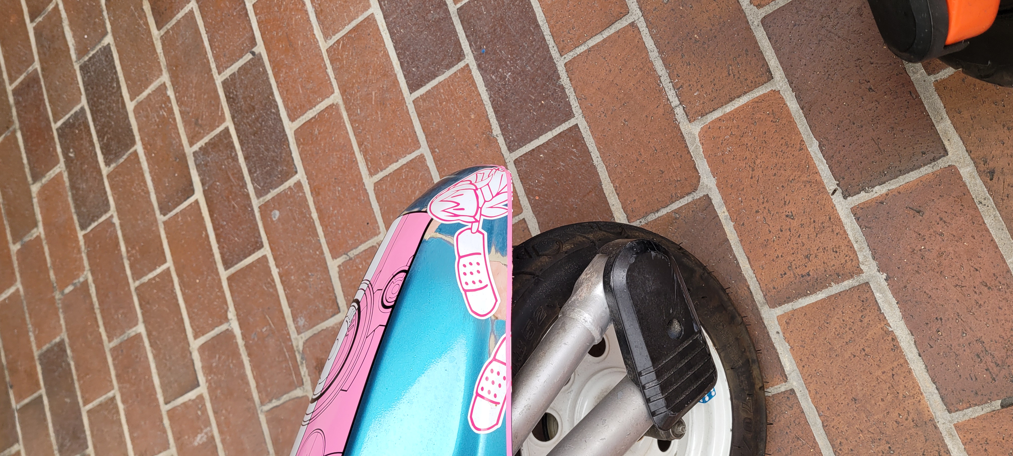 a close-up photo of the luka itasha bike. it shows the area near the front wheel of the bike, where pink and white bandage decals cover up cosmetic damage to the bike. a small cute luka is seen applying the bandages.