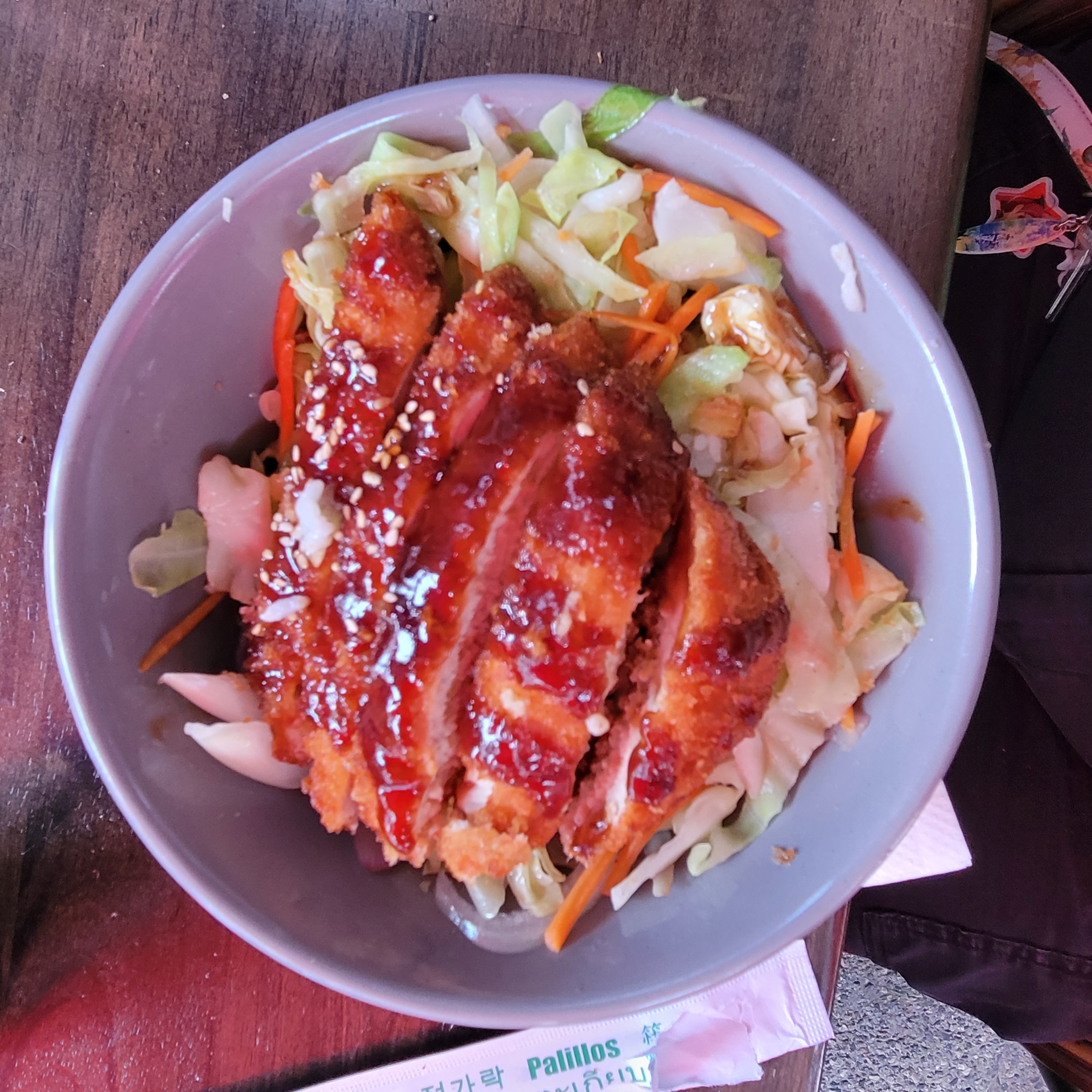 a photo of a chicken teriyaki bowl. chicken katsu covered in teriyaki sauce and sesame seeds sits in the bowl atop a bed of lightly pickled vegetables and white rice.