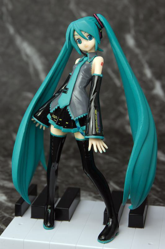 an early prize figure of miku, released in 2008. she is standing on the keys of a piano.
